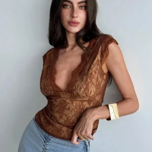 Brun spetsblus med v-ringning - Säljer en brun, transparent spetsblus med djup v-ringning och fina spetsdetaljer längs kanterna. Blusen är ärmlös och har en figurnära passform, perfekt att styla med jeans eller kjol. Superfin och trendig topp! Sitter jättefint på kroppen. Ej använd bara provats en gång. 