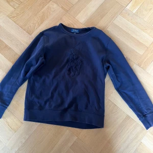 Polo Ralph Lauren - Mörkblå sweatshirt från polo Ralph Lauren. Sweatshirt med broderad stor logga på bröstet. Tröjan har rund halsringning och långa ärmar. Perfekt för en sportig och avslappnad stil.