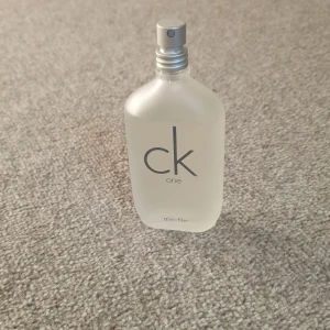 CK One Eau de Toilette från Calvin Klein - Fräsch och ikonisk unisexparfym från Calvin Klein, CK One. Flaskan är frostad och genomskinlig med minimalistisk design och silverfärgad spraykork. Levereras med originalförpackning.