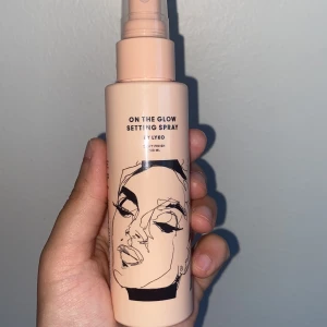 On The Glow Setting Spray - On The Glow Setting Spray från Lyko i en ljusbeige plastflaska med svart konstnärlig illustration. Ger en dewy finish och håller sminket på plats. Innehåller 100 ml och är enkel att applicera med spraymunstycke.