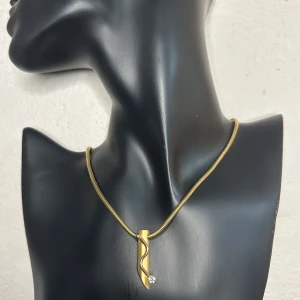 Vintagehalsband med skulpturalt hänge med gnistrande sten Retro 80-tal 90-tal - Skulpturalt vintagehalsband i guldfärgad metall med asymmetriskt hänge och liten klar sten. Kedjan är ca 42 cm lång, hänget ca 3,5 cm. Troligen från sent 80-/tidigt 90-tal. Ett stilrent smycke i mycket fint vintage-skick – perfekt för både vardag och fest.  Ingen prutning, men jag erbjuder gärna bundlerabatt. Jag rensar smyckesskrin och garderob – kika gärna på mina andra annonser också! 