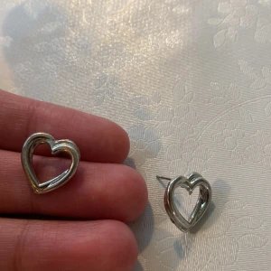 Silverfärgade hjärtformade örhängen - Säljer ett par örhängen i silverfärg med hjärtformad design. Säljer eftersom jag föredrar guld smycken och inte silver längre!❤️Har används kanske 4 gånger ungefär. Jag tvättar örhängen innan jag skickar iväg den❤️