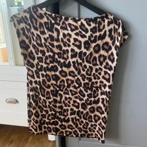 Leopardmönstrad topp - Säljer en snygg topp med leopardmönster. Toppen har korta ärmar och är tillverkad i ett mjukt, syntetiskt material. Perfekt för dig som vill sticka ut med ett djurmönster!