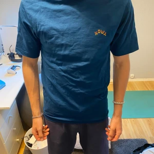 Blå t-shirt från Nowa med tryck - Säljer en blå t-shirt från Nowa med coolt tryck på ryggen av en hand och texten NOWA. T-shirten har normal passform och korta ärmar. Perfekt för dig som vill sticka ut med en unik design. Säljer för att den inte är min still längre 