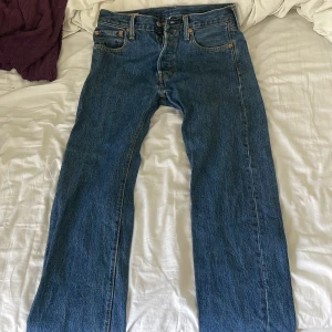 Levi's 501 blå jeansbyxor W30 L30 - Klassiska blå Levi's 501 jeans med raka ben och femficksmodell. Byxorna har knappgylf och är tillverkade i slitstarkt denim. Ikonisk läderpatch bak i midjan och röd Levi's-tagg på bakfickan. Perfekta för en tidlös stil.
