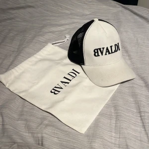 Vit och svart keps från BVALDI - Snygg vit keps med svart nätpanel från BVALDI. Kepsen har en broderad logotyp framtill och justerbar passform. Nypris 500 kr. Endast använd ett fåtal gånger. Liten fläck på höger sida av skärmen som syns i bilden men annars helt felfri.