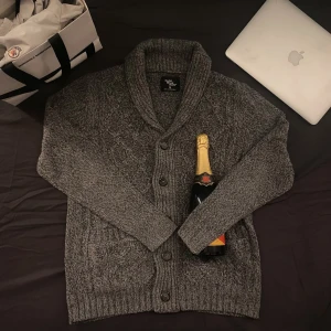 Grå kofta från Cedar Wood State - Säljer en snygg grå kofta från Cedar Wood State. Koftan har ett klassiskt mönster och knappar framtill. Perfekt för kyligare dagar med sin mysiga och stilrena design.