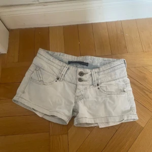 Lowwaist ljusblå shorts - Säljer ett par lowwaist shorts med dubbla knappar framtill. De har en klassisk femficksdesign och är perfekta för sommardagar. Shortsen är lågmidjade och har en stilren look.