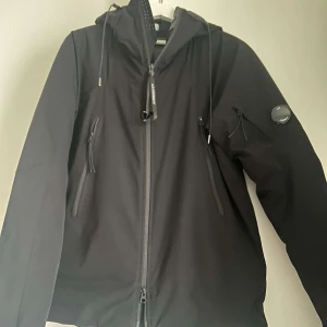 Svart jacka från C.P. Company - Snygg svart jacka från C.P. Company med dragkedja och flera praktiska fickor. Jackan är lite tjockare så perfekt för en kall kväll. Storlek M 