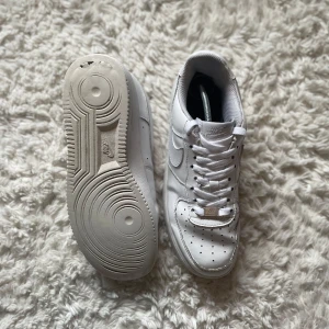 Vita Nike Air Force sneakers - Säljer ett par klassiska vita Nike Air Force sneakers. De har en stilren design med snörning och perforerade detaljer på tån för extra ventilation. Perfekta för en casual look.