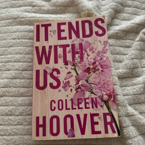 It Ends With Us - Boken 'It Ends With Us' av Colleen Hoover är en gripande roman som utforskar kärlekens komplexitet och de svåra valen i livet. Omslaget pryds av en vacker rosa blomma mot en träliknande bakgrund. Perfekt för dig som älskar känslosamma och tankeväckande berättelser.