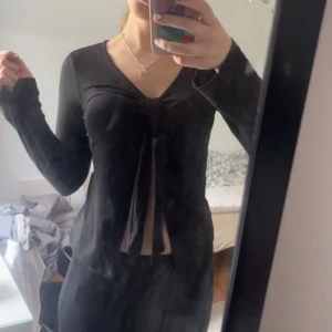 Svart långärmad topp med knyt, ginatricot - Snygg svart långärmad topp med knyt framtill. Perfekt för en stilren look. Toppen har en v-ringad design som ger en elegant touch. Använts endast 2 ggr.