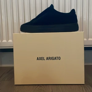 Svarta sneakers från Axel Arigato - Snygga svarta sneakers från Axel Arigato med en minimalistisk design. Skorna har en stilren look utan snörning och är perfekta för en modern stil. De är tillverkade i ett material som ger en lyxig känsla.