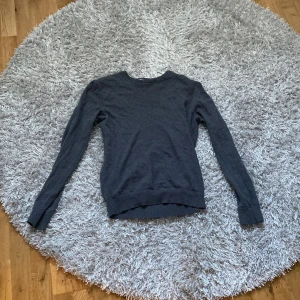 Grå tröja från Pier One - Säljer en stilren grå tröja från Pier One. Tröjan har långa ärmar och en klassisk rund halsringning med en vit och marinblå randig detalj på insidan av kragen. Perfekt för en avslappnad look.