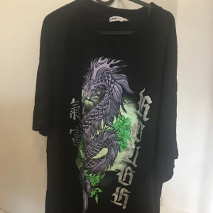 Svart t-shirt med draktryck - Cool svart t-shirt med ett stort draktryck i lila och grönt på framsidan. Strl XL med oversized passform