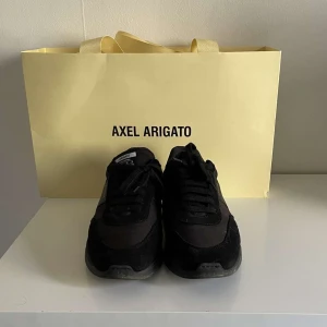 Svarta sneakers från Axel Arigato - Snygga svarta sneakers från Axel Arigato med en stilren design. Skorna har en robust sula och är tillverkade i en kombination av mocka och syntetmaterial. Perfekta för en trendig look. Skorna är knappast använda