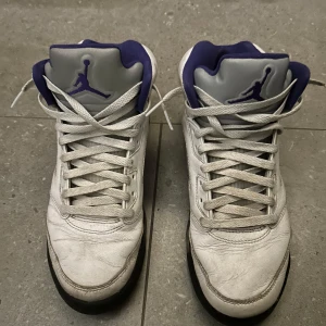 Air Jordan 5 - Säljer ett par klassiska vita Nike Air Jordan 5 med lila detaljer. Perfekta för sneakerheads som vill ha en stilren look med en touch av färg. Dom är väl använda men fungerar utmärkt. Hör gärna av er med frågor eller funderingar!