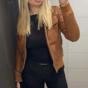 Brun skinnjacka från MNG Collection - Säljer en snygg brun skinnjacka från MNG Collection. Jackan har en dragkedja framtill och två fickor med lock på bröstet. Den har en klassisk krage och ribbade muddar vid ärmslut och nederkant. Köpt secondhand. I storlek M men passar mer som en S🤍
