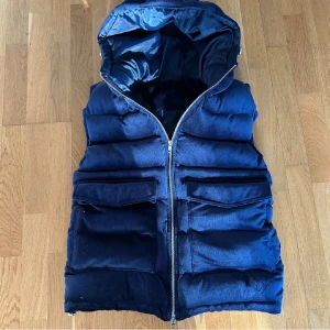 Vendiera väst  - Snygg mörkblå dunväst med dragkedja och huva. Perfekt för kyliga dagar. Västen har flera praktiska fickor framtill. Knappt använd och väldigt skönt material