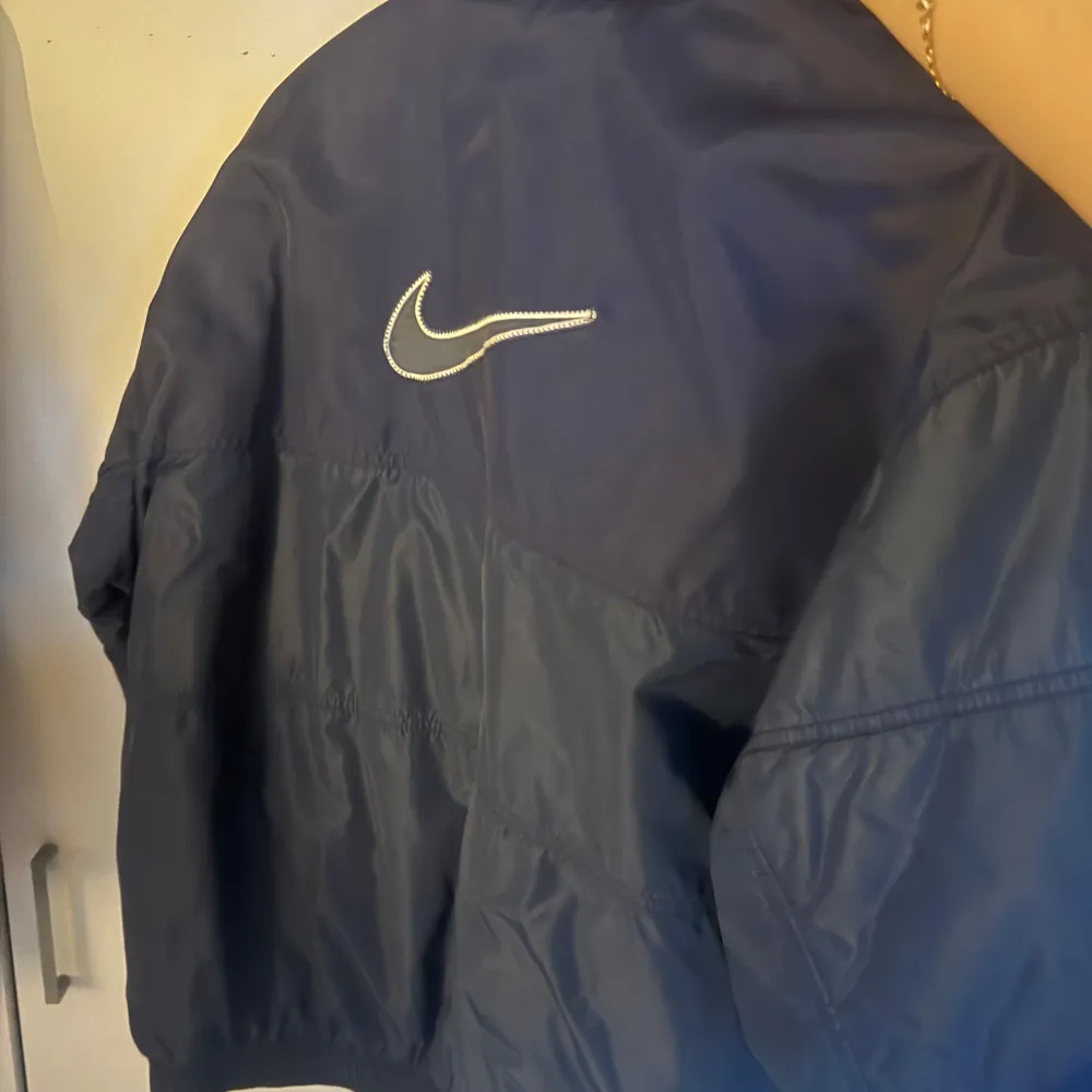 Säljer en blå pufferjacka från Nike med dragkedja och tryckknappar. Jackan har långa ärmar och en stilren design med Nike-logga på bröstet och ryggen. Perfekt för kyligare dagar. Strl M. Takit.