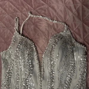 Silverfärgad paljettklänning - Säljer en fantastisk silverfärgad långklänning med paljetter och djup v-ringning. Klänningen har smala axelband och en figurnära passform som ger en elegant look. Perfekt för en glamorös kväll!