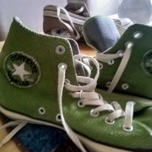 Gröna Converse All Star sneakers - Säljer ett par gröna Converse All Star sneakers med klassisk hög design och vita snören. Skorna har den ikoniska stjärnloggan på sidan och en vit sula med svart text. Perfekta för en avslappnad stil.