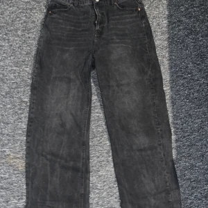 Svarta jeansbyxor från H&M - Snygga svarta jeansbyxor från H&M med en klassisk design. Byxorna har en rak passform och är perfekta för en avslappnad stil. De har fickor både fram och bak samt en knapp och dragkedja i gylfen.