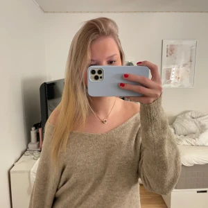 Beige stickad offshoulder tröja - Säljer en mysig beige stickad tröja med offshoulder-design. Perfekt för kyliga dagar med sin mjuka och bekväma passform. Tröjan har långa ärmar och ribbade muddar.