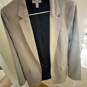 Beige kavaj - Snygg beige kavaj med klassisk design. Perfekt för att ge en stilren touch till din outfit. Kavajen har en elegant passform och är tillverkad i ett mjukt material.