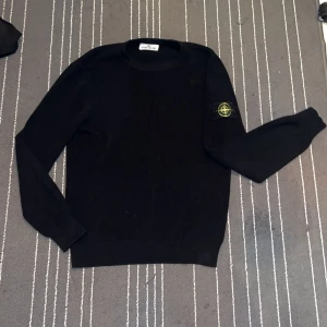 Svart tröja från Stone Island - Säljer en stilren svart tröja från Stone Island med deras ikoniska märke på ärmen. Tröjan har en klassisk passform och är perfekt för en avslappnad look. Den är tillverkad i ett mjukt material som ger en skön känsla. Perfekt för dig som gillar enkel och tidlös design.