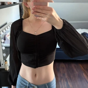 Svart långärmad topp - Säljer en snygg svart topp med långa ärmar och en smickrande v-ringad design. Toppen är croppad och har en åtsittande passform som framhäver figuren. Perfekt för en stilren look.