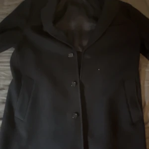 Svart ullrock från arket  - Elegant svart ullrock med knappar framtill. Tillverkad av italienskt tyg, perfekt för en stilren look. Kappan har en klassisk design med långa ärmar och en slät yta. Pris kan diskuteras vid snabb och smidig affär!