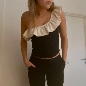 Svart offshoulder topp med volang - Säljer en stilren svart offshoulder topp med en snygg volangdetalj i beige längs kanten. 💘💘