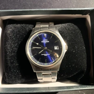 Silverfärgad klocka från Tidema - Snygg silverfärgad klocka från Tidema med blå urtavla och datumvisning. Armbandet är i metall och klockan levereras i en vit låda med extra länkar. Perfekt för den som gillar stilrena accessoarer.  priset går och handlas