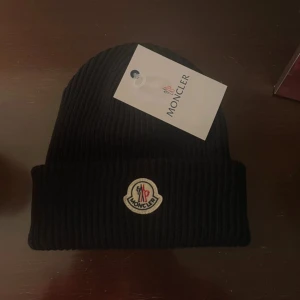 Svart Moncler Mössa - Snygg svart ribbad mössa från Moncler med deras ikoniska logotyp framtill. Perfekt för att hålla värmen under kyliga dagar. Stilren design som passar till det mesta. Helt ny. Pris kan diskuteras!