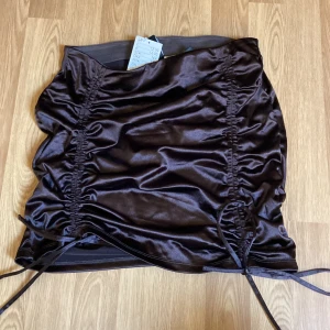 Brun satin kjol, Hm - Brun satin kjol från Hm med snöre på sidorna, prislappen är kvar, den är helt ny och aldrig använd man kan justera snören så kjolen blir kort o lång 💕funkar även bra för de som har storlek s, passar mig och jag har storlek xs-s 