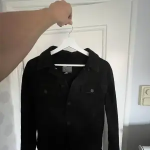 Snygg svart jacka med knappar framtill och klassisk krage. Perfekt för en stilren look. Jackan har två bröstfickor med knappar.