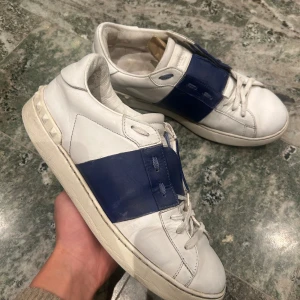 Valentino Garavani sneakers i vitt och blått - Snygga Valentino Garavani sneakers i vitt skinn med en bred blå rem över snörningen. Skorna är i helt okej skick och inget extra ingår! Storlek 43
