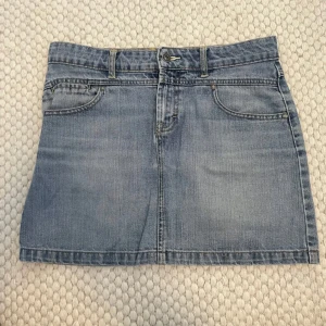 Blå jeanskjol - Snygg blå jeanskjol med klassisk femficksdesign och bälteshällor. Perfekt för en avslappnad stil. Kjolen har en knapp och dragkedja framtill.
