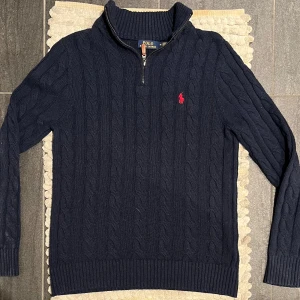 Polo Ralph Lauren Cable Knit Half Zip Tröja Navy - Säljer en snygg mörkblå stickad tröja från Polo Ralph Lauren med dragkedja och ribbad krage. Tröjan är i storlek M. Använd men i fint skick, något nopprig 