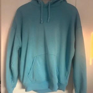 Blå hoodie med ficka - Säljer en snygg blå hoodie med känguruficka och justerbar huva. Perfekt för en avslappnad stil. Passar bra till både jeans och mjukisbyxor.