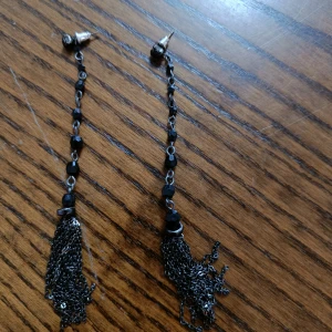 Långa svarta örhängen med kedjor - Säljer ett par coola långa örhängen med svarta pärlor och silverfärgade kedjor som hänger i tofsar. Perfekt för dig som vill sticka ut med en edgy och unik stil. Passar till både street och lite mer dressade looks.