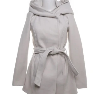 Vit kappa med huva från Amisu - Snygg vit kappa från Amisu med stor huva och knytskärp i midjan. Jackan har en stilren design, är långärmad och tillverkad i mjuk polyester. Perfekt för dig som vill ha en clean och trendig look under kyliga dagar.