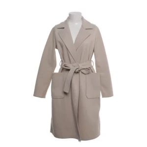 Beige kappa med bälte från Amisu - Snygg beige kappa från Amisu i storlek 36. Modellen har klassisk krage, stora fickor framtill och ett matchande bälte i midjan. Jackan är tillverkad i mjuk polyester och har långa ärmar. Perfekt för dig som gillar stilrena och enkla plagg.
