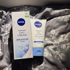 Nivea Day Cream 24H Moisture SPF 15 - Nivea Refreshing Day Cream med 24H fukt, vitamin E och SPF 15 för normal hud. Kommer i en vit tub med blå detaljer och tillhörande kartong. Vegansk formula som ger återfuktning och skydd mot solen.