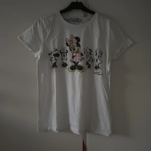 Vit Disney t-shirt med Minnie Mouse - Vit t-shirt med tryck av Minnie Mouse i olika stilar framtill. T-shirten har rund hals, korta ärmar och är gjord i mjuk bomull. Perfekt för dig som älskar Disney och vill ha en chill och lekfull vibe i din outfit.
