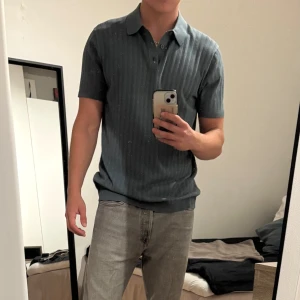 Grön ribbad pikétröja från KappAhl - Grön pikétröja från KappAhl i storlek M. Tröjan har korta ärmar, klassisk krage och knäppning framtill. Den är ribbad med diskreta vertikala ränder. Använd en gång.