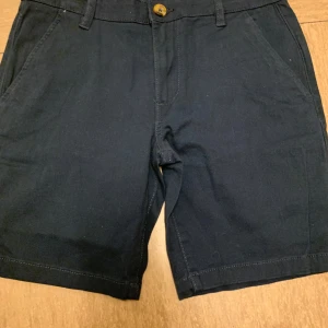 Mörkblå shorts från 157 Lee Star - Snygga mörkblå shorts från 157 Lee Star med klassisk rak passform och midwaist. De har fickor fram och bak, bälteshällor och stängs med knapp och dragkedja. Materialet är mjuk bomull som känns skönt mot huden. Perfekta för varma sommardagar och chill häng.