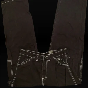 Svarta cargopants med vita sömmar - Svarta cargopants med kontrasterande vita sömmar och flera stora fickor på sidorna. Byxorna har raka ben och klassisk cargostil med bälteshällor och dragkedjegylf. Perfekta för en streetwear-look och riktigt snygga detaljer. Knappen är lite lös dock.