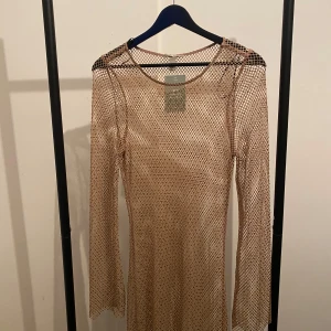 Beige nätklänning från H&M XS - Säljer en beige långärmad nätklänning från H&M i storlek XS. Klänningen är gjord av 97% återvunnen polyester och har ett coolt meshmönster som ger en edgy vibe. Perfekt för dig som gillar transparenta lager och vill sticka ut.